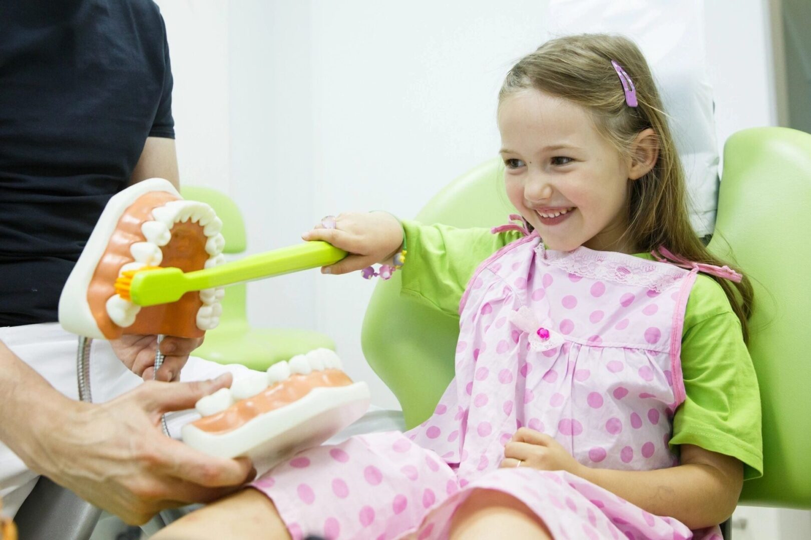 A little girl in pink pajamas getting food from a person.